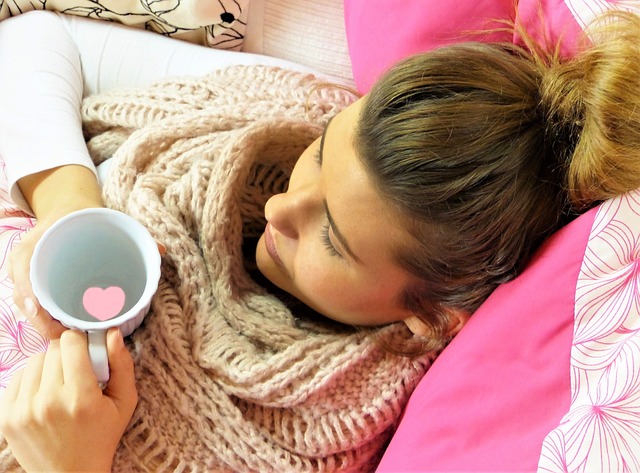 Sick woman holding a cup of tea lying in bed